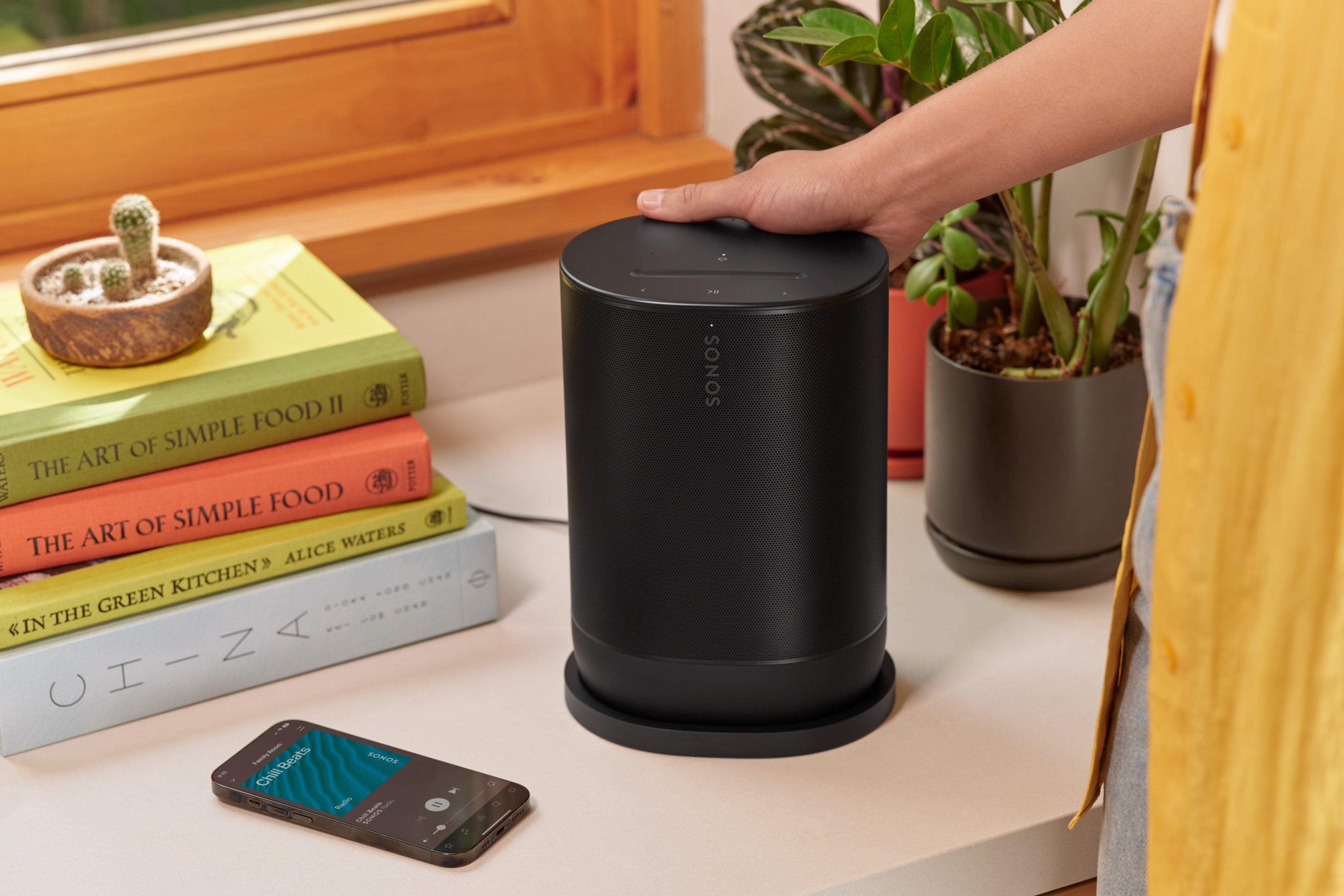 Obraz Sonos Move 2 w kolorze czarnym, stawianego na podstawie ładującej obok stosu książek i iPhone’a