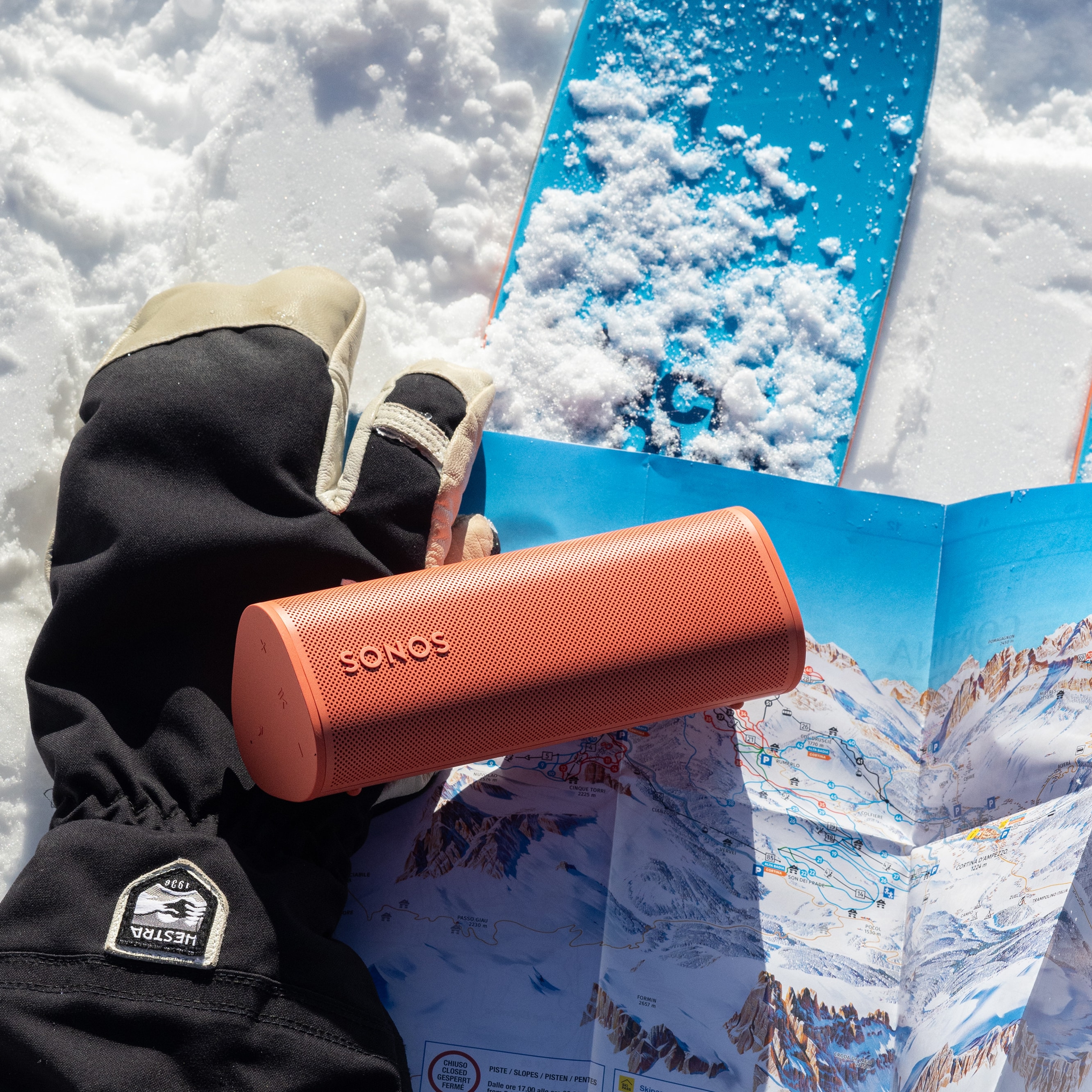 Ein Roam 2 in Rot auf einem Handschuh mit Skiern im Schnee
