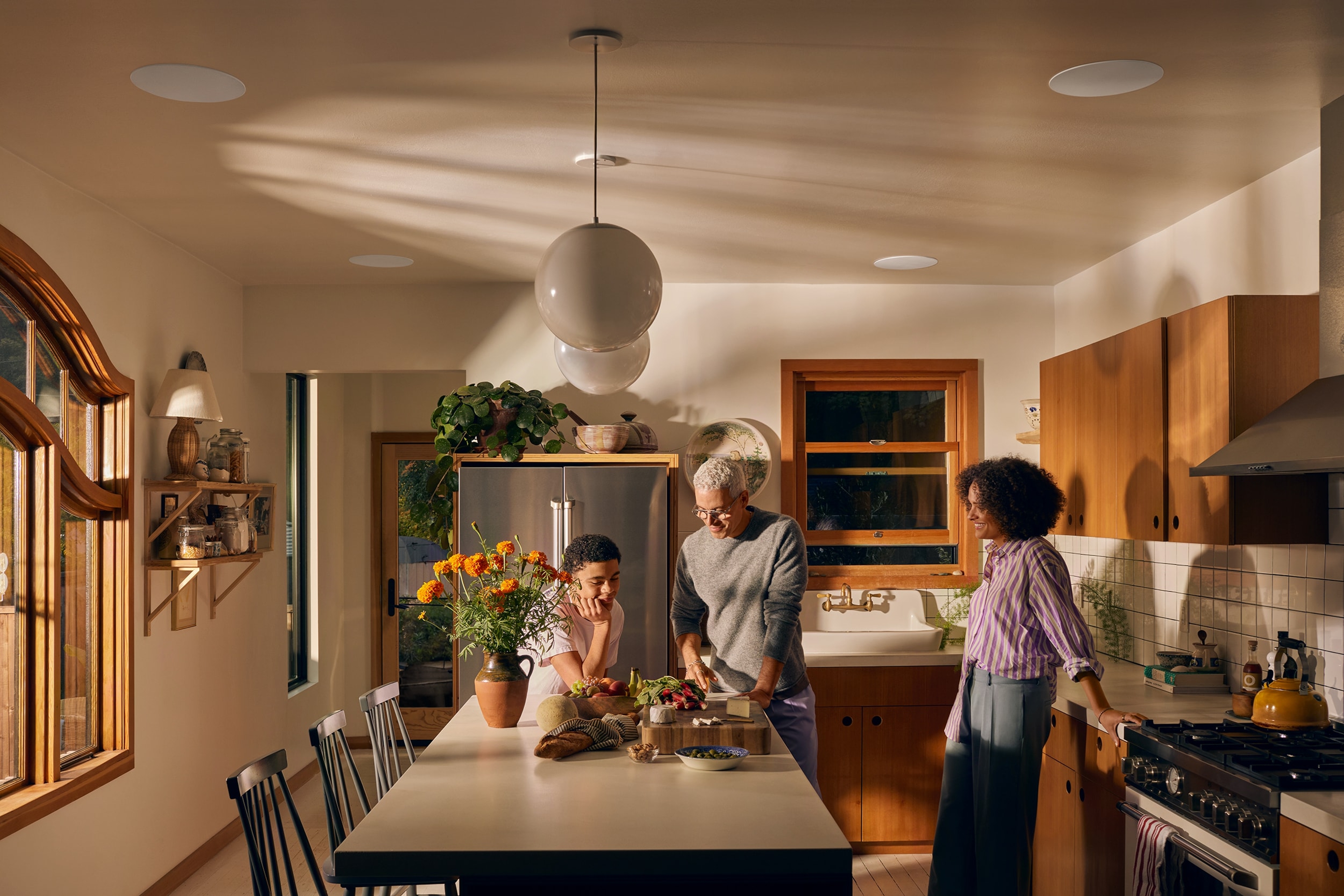 Una familia en una cocina con altavoces In-Ceiling de Sonance instalados encima de una isla