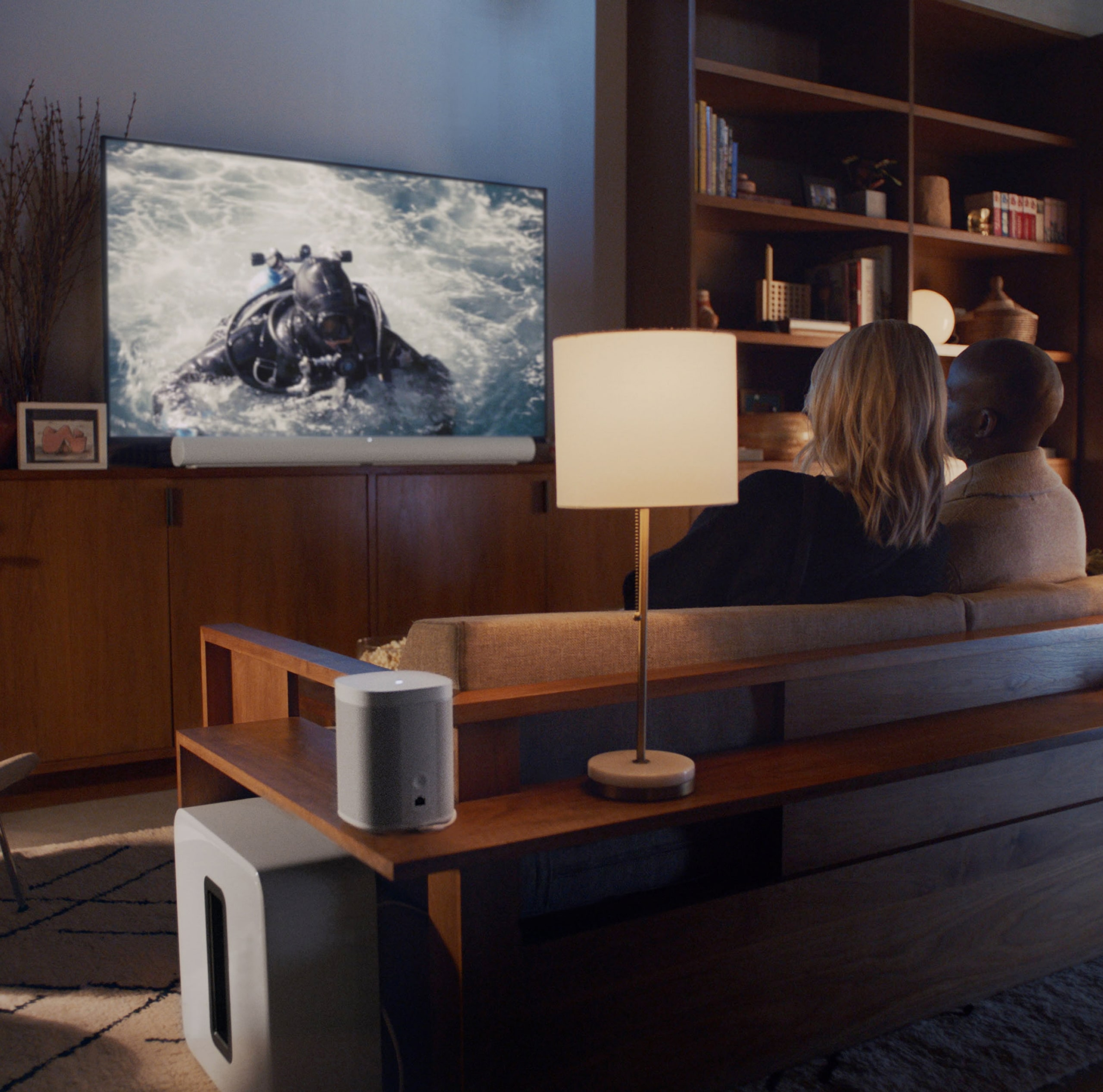Couple watching TV with white Sonos Arc home cinema system