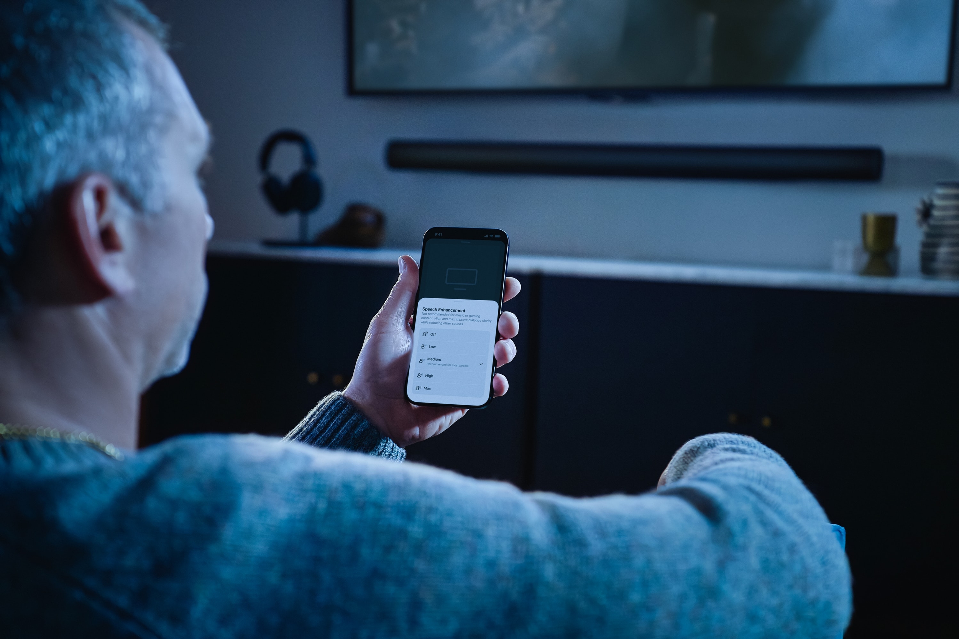 En person som tittar på Sonosappen på sin telefon med Arc Ultra i bakgrunden