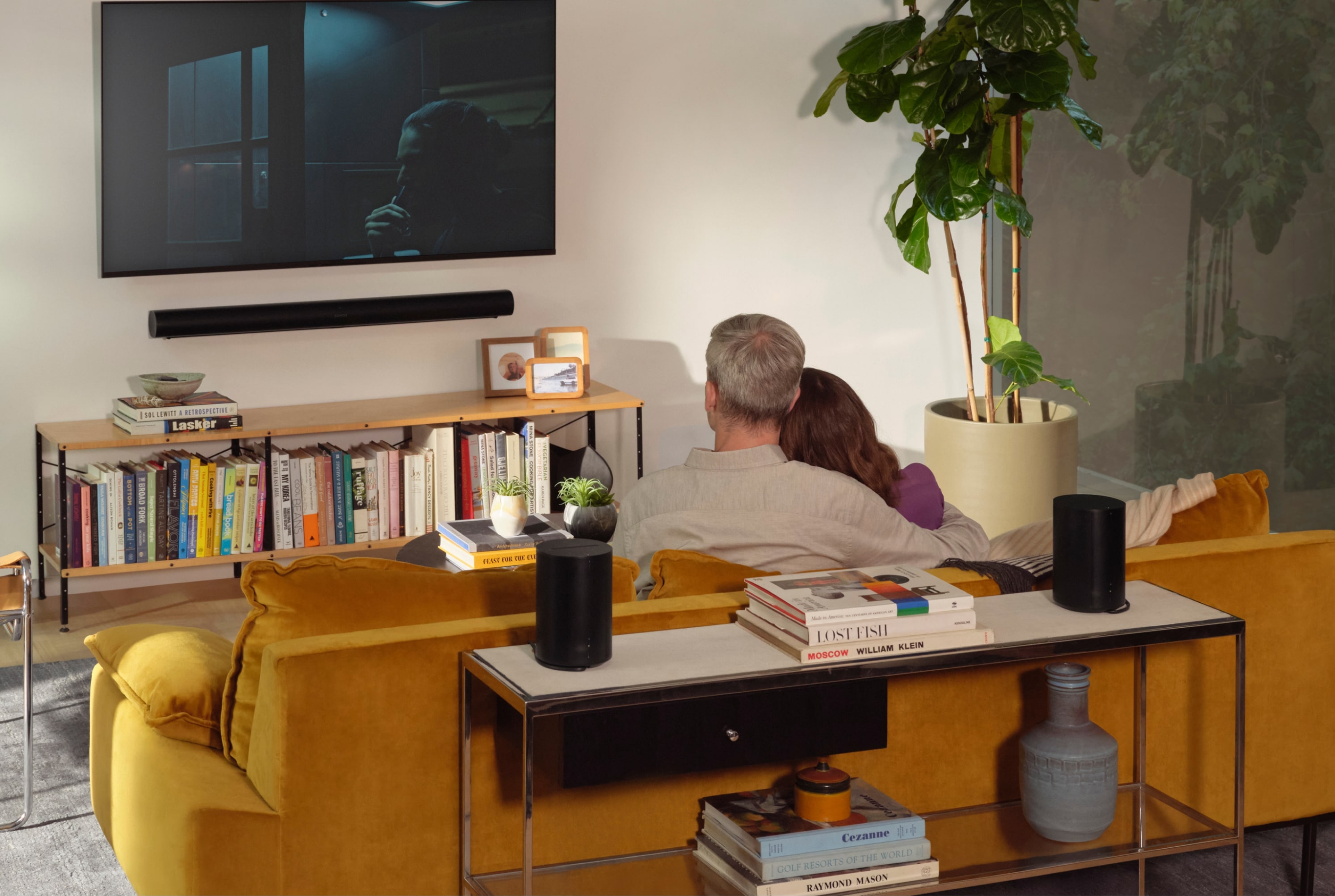 Un couple qui écoute un ensemble ambiophonique avec Arc et Era 100 de Sonos dans un salon.