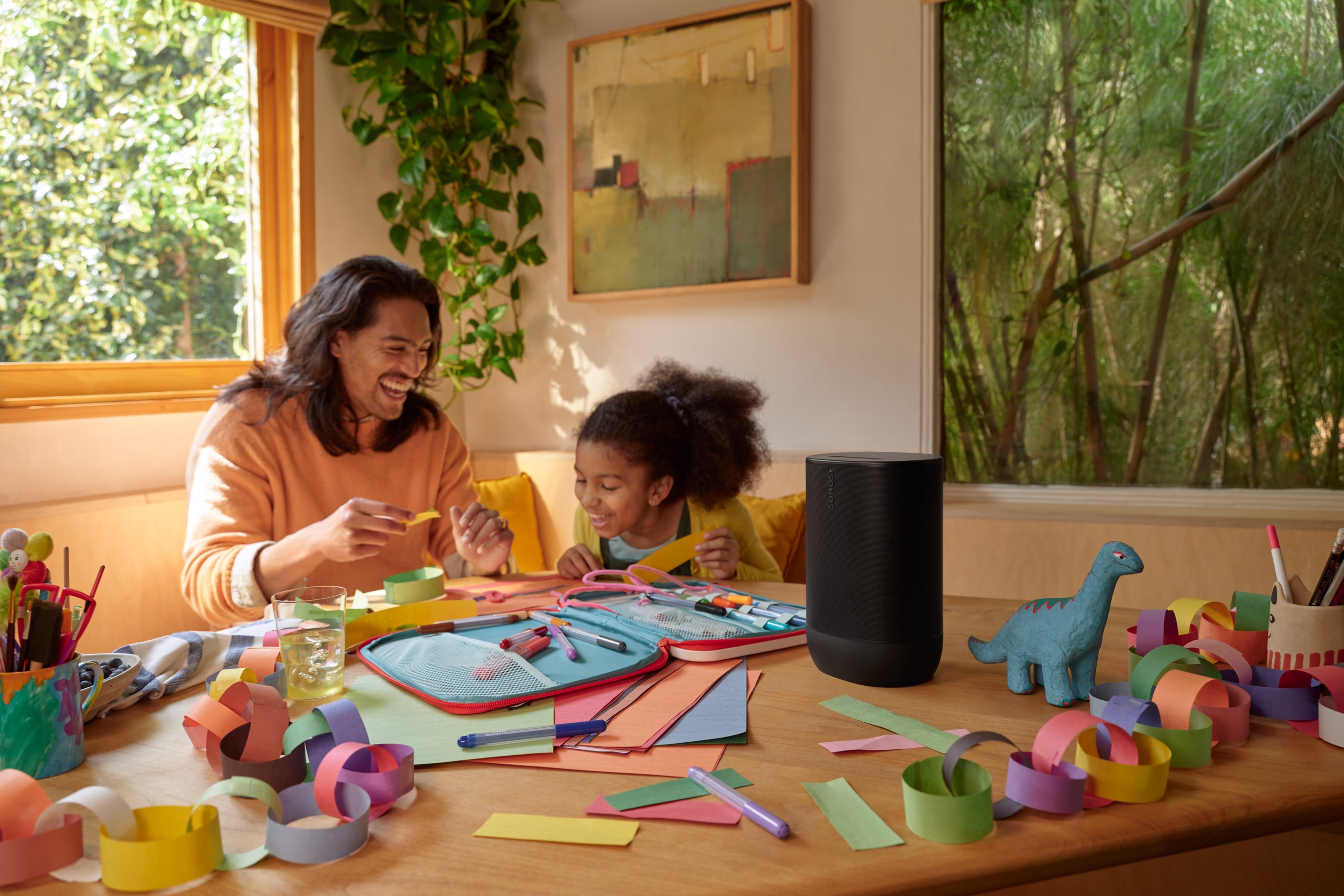 Photo d'un père et de sa fille à la table de la cuisine en train de bricoler tout en écoutant de la musique diffusée par un Sonos Move 2 noir