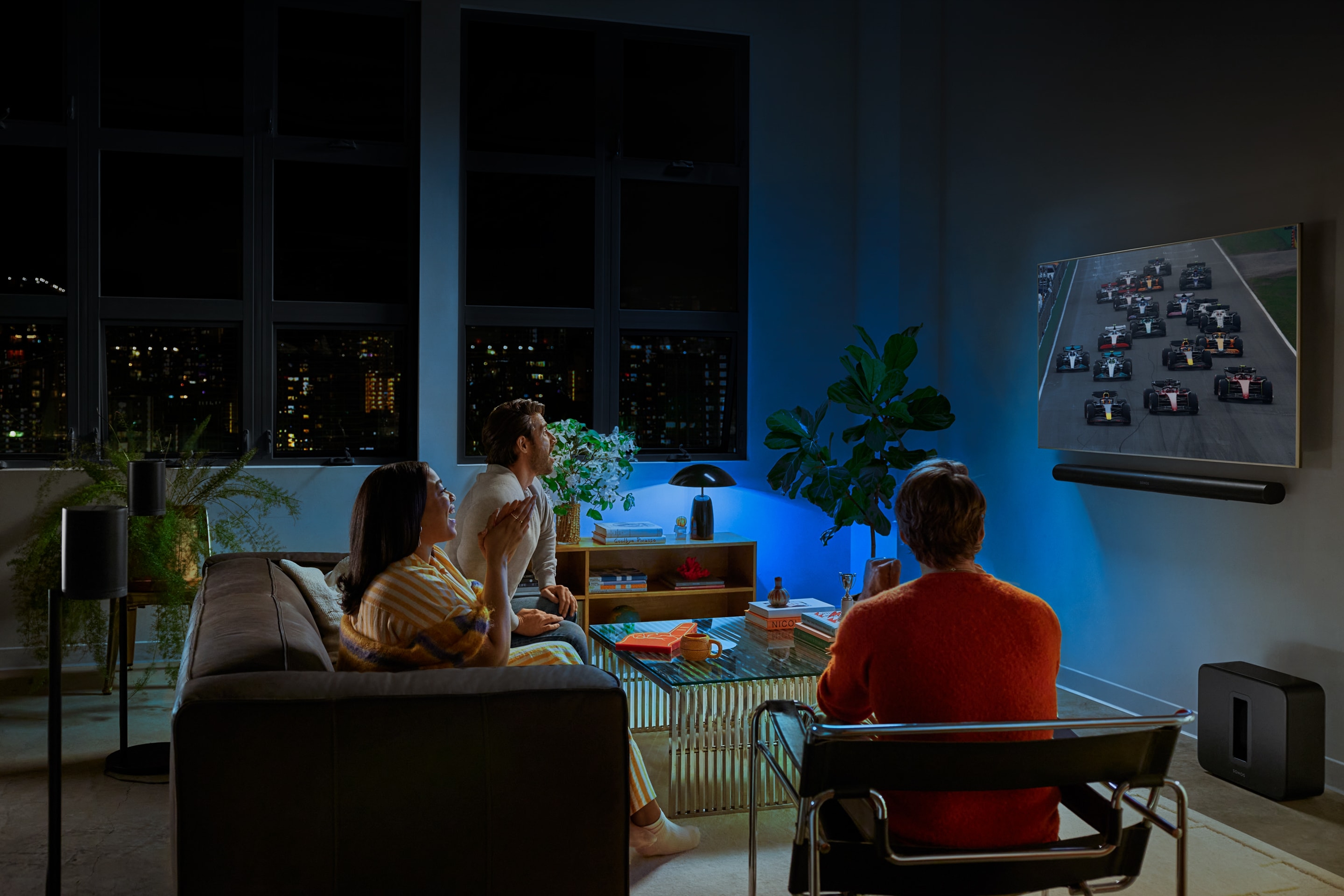Un groupe d'amis en train de regarder la F1 avec un système home cinéma Sonos et un éclairage Philips Hue bleu
