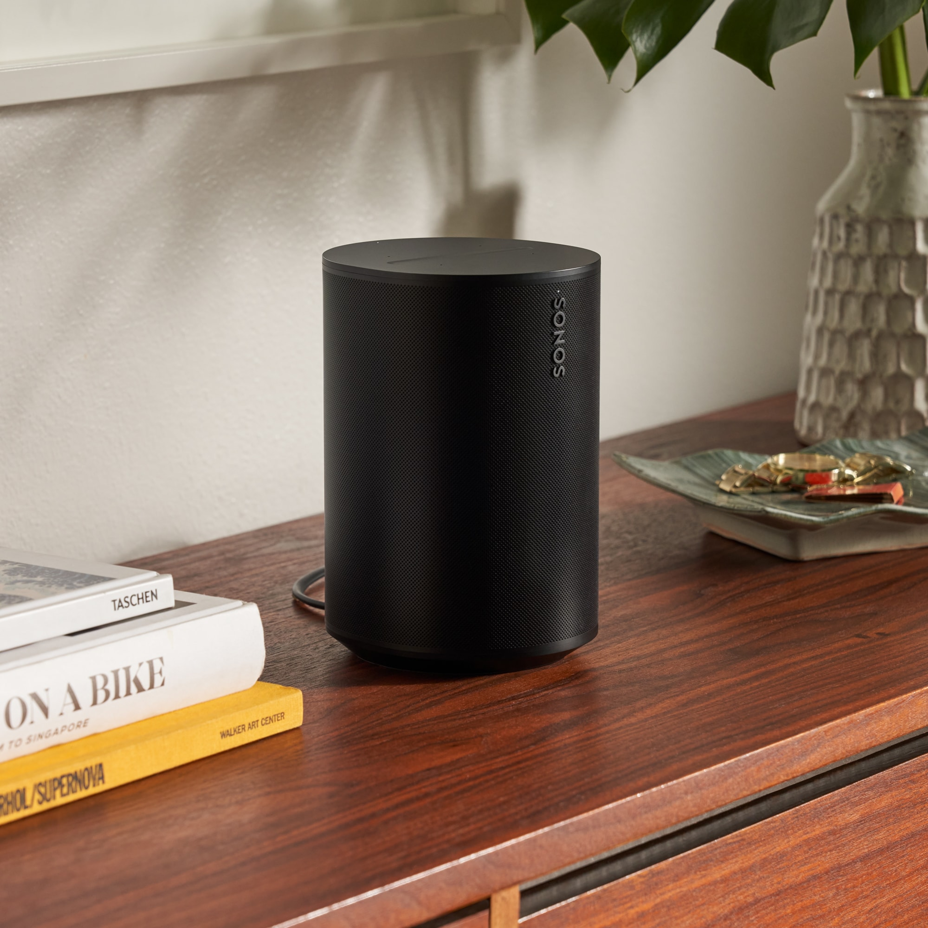 Une enceinte Sonos Era 100 noire sur un buffet à côté de livres et d'un vase