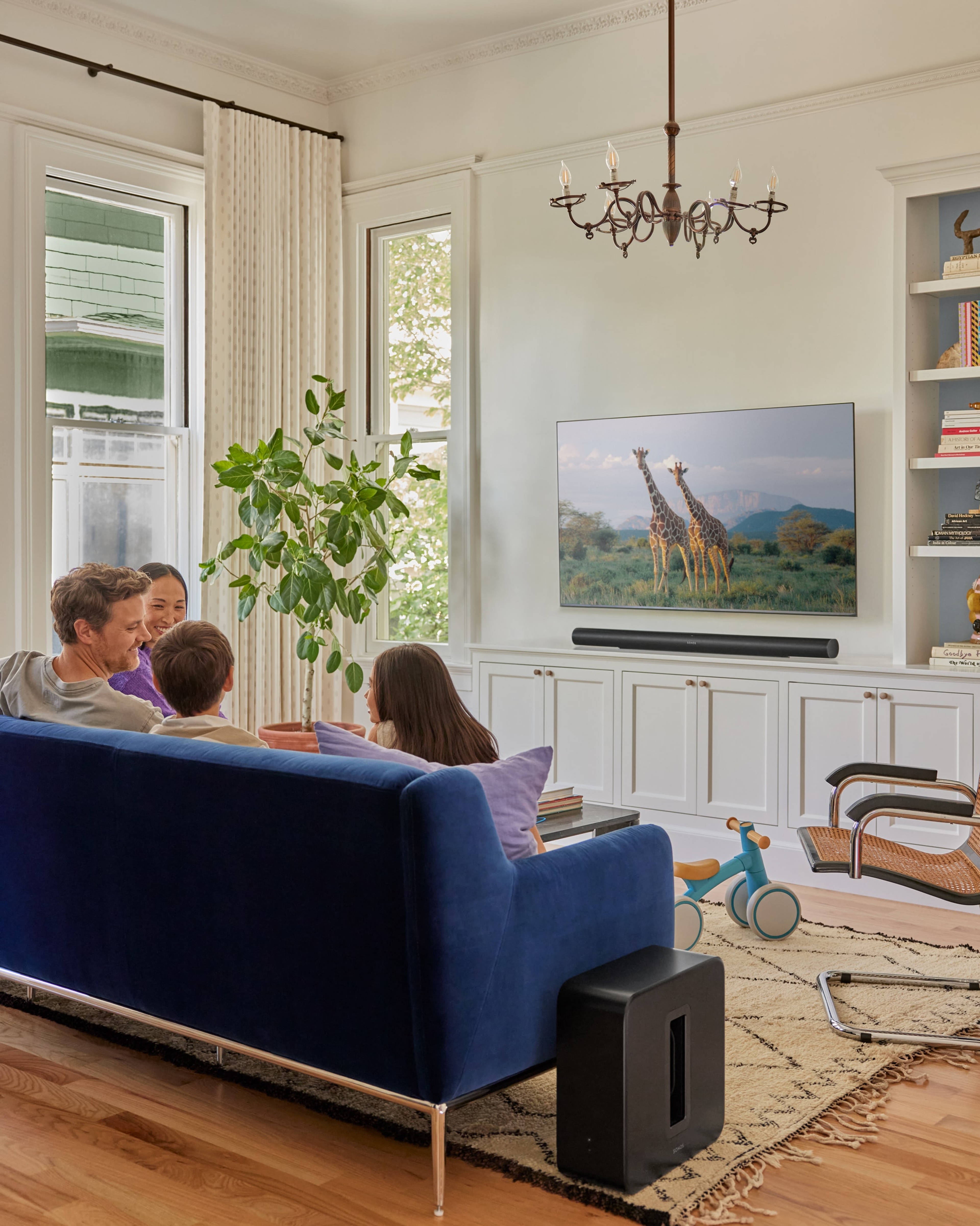 Rodzina siedząca na niebieskiej kanapie w salonie z Sonos Sub 4 i Arc Ultra