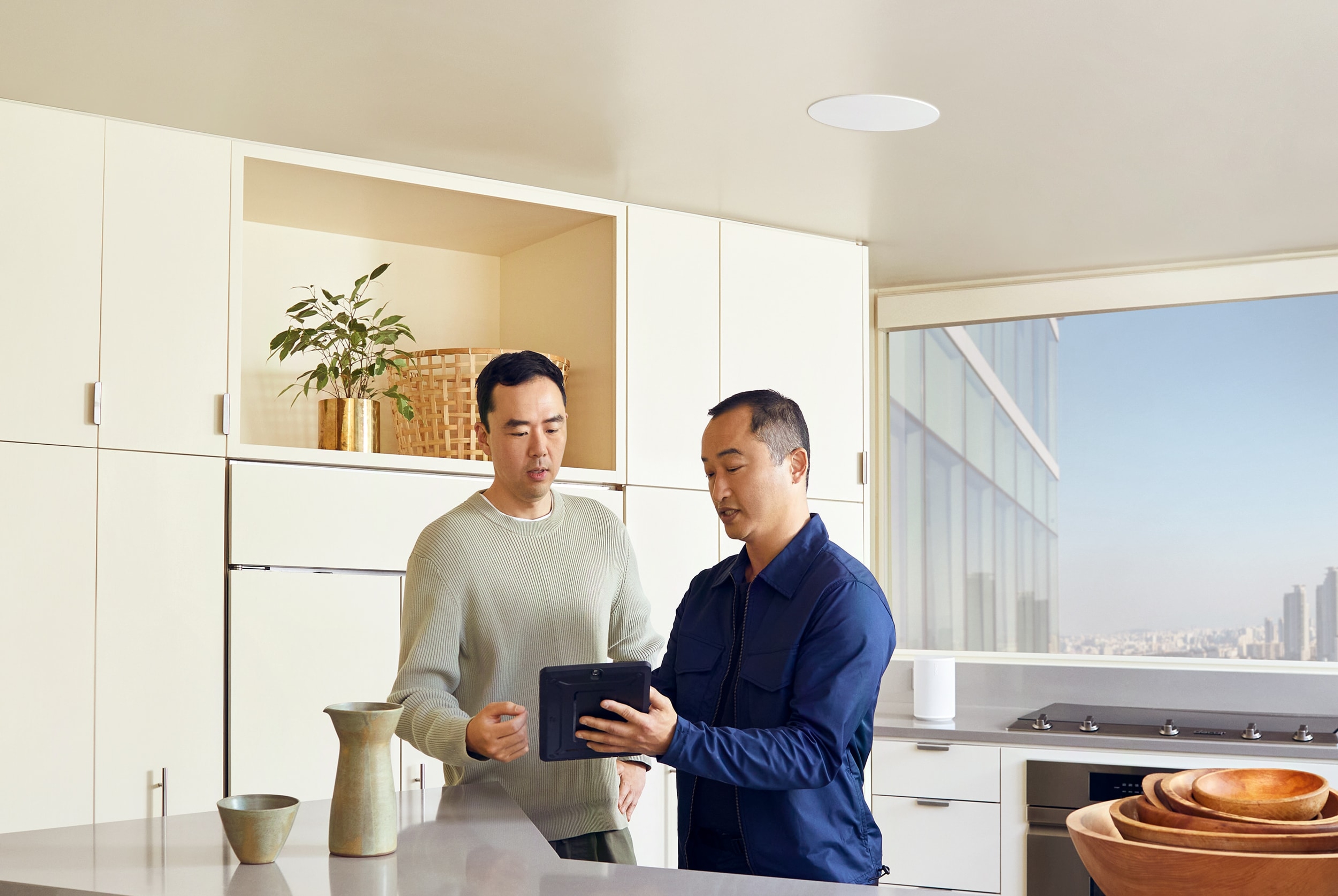 Dos hombres charlando en la cocina con los altavoces Sonos In-Ceiling de Sonance instalados encima de una isla de cocina