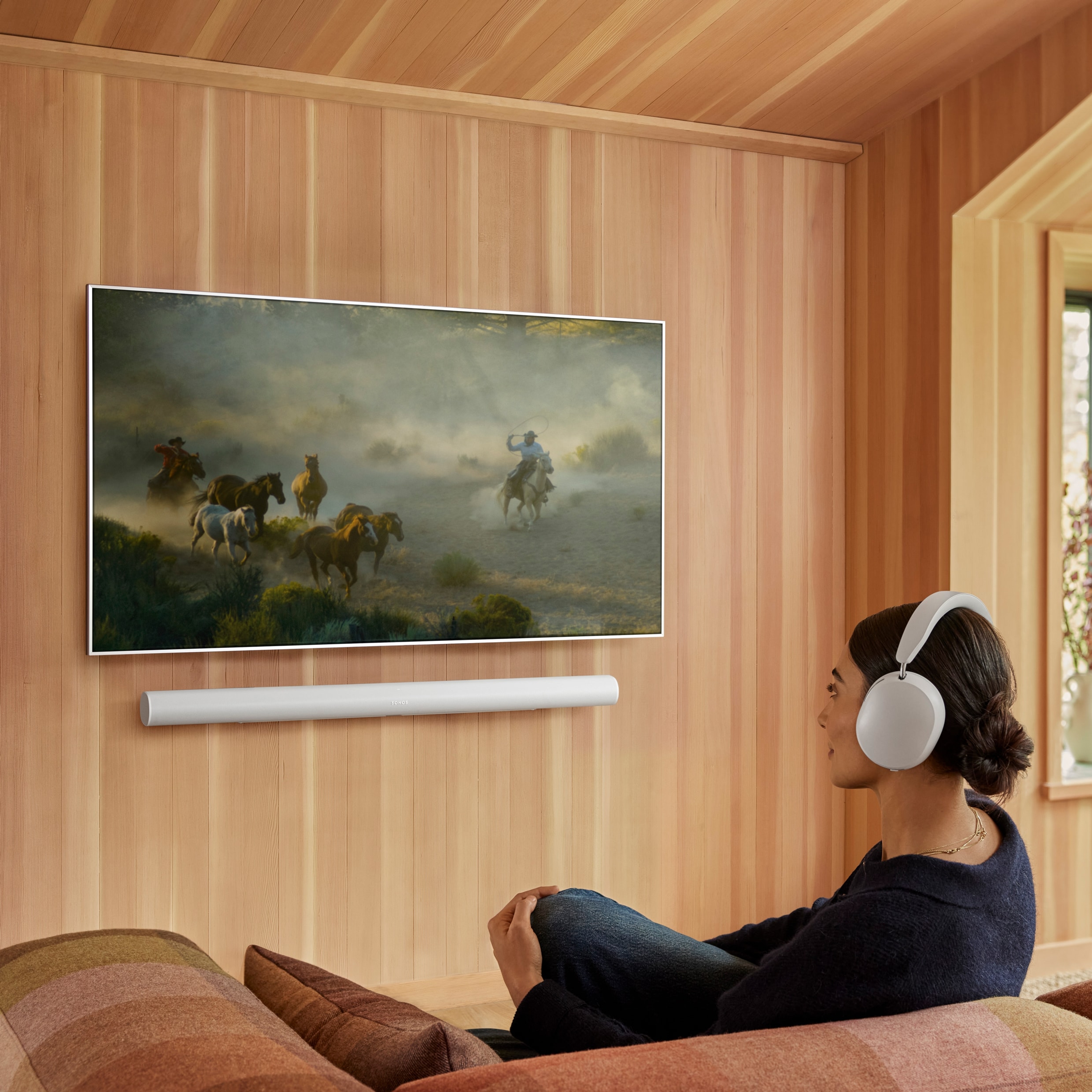 Eine Frau auf einer Couch, die die Funktion Sound Swap nutzt, um Sound von einer Arc Ultra in Weiß auf ihren Sonos Ace zu wechseln