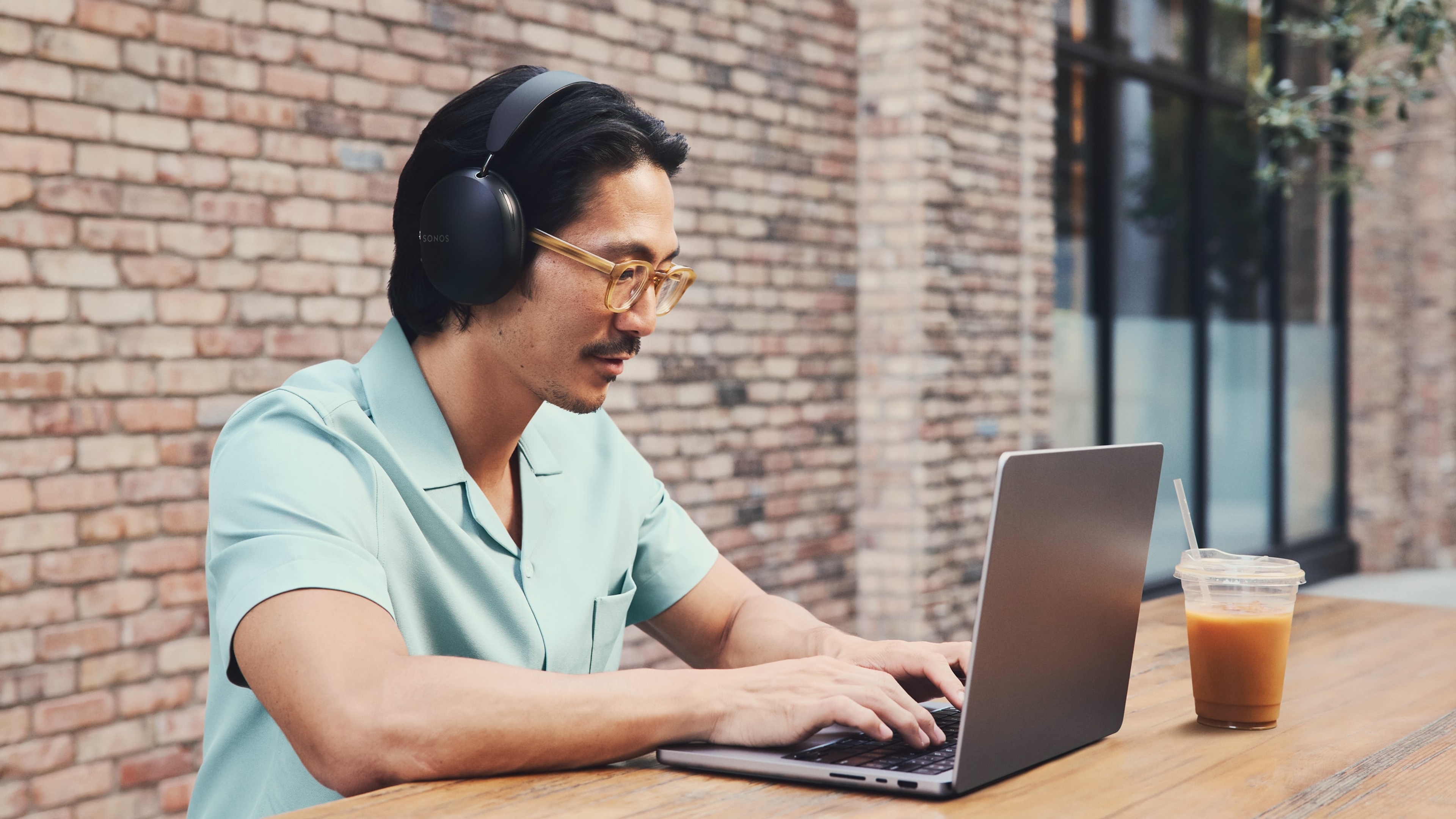 Osoba przed kawiarnią z czarnymi słuchawkami Sonos Ace pracuje na laptopie