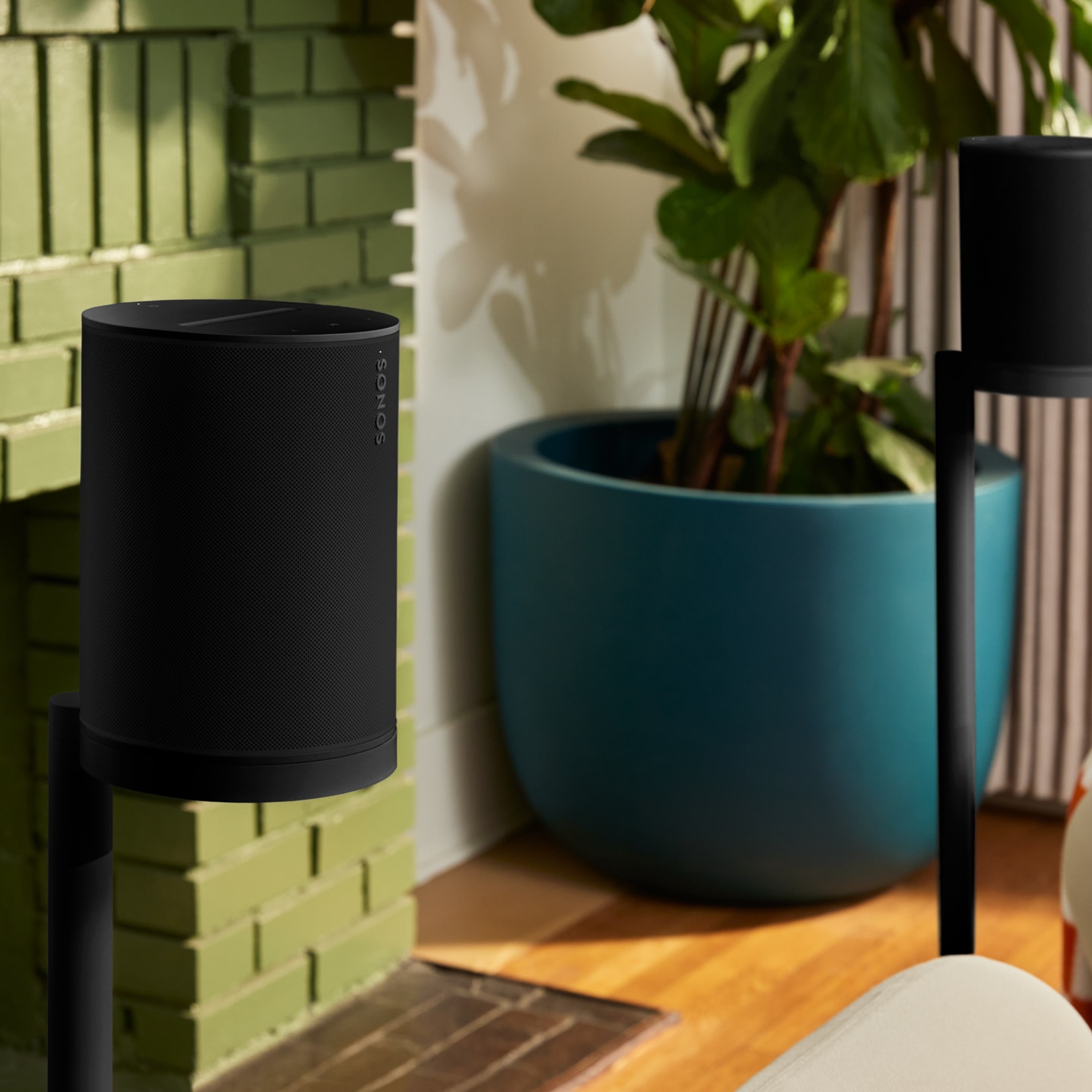 Un par de bocinas Sonos Era 100 SL en color negro en sus correspondientes soportes de pie reproducen sonido surround en una sala