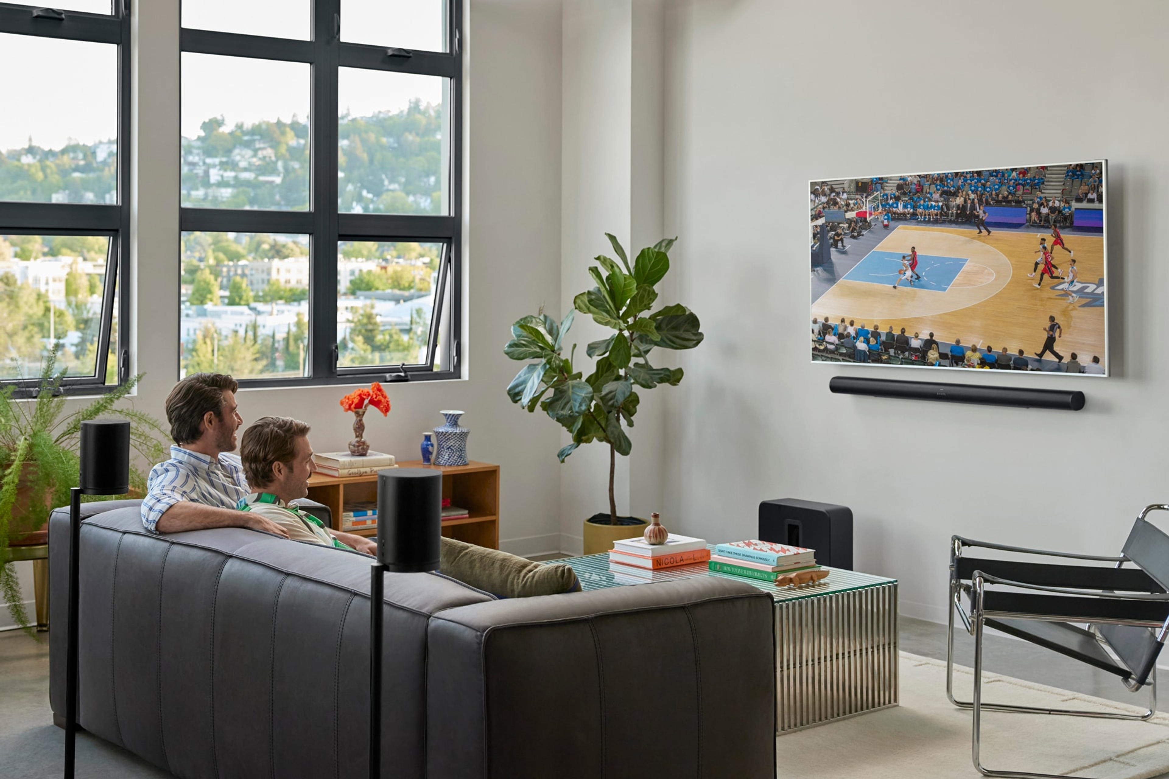Couple watching basketball on the couch with an Arc Ultra, Sub 4, and pair of Era 100 SL speakers for surround sound
