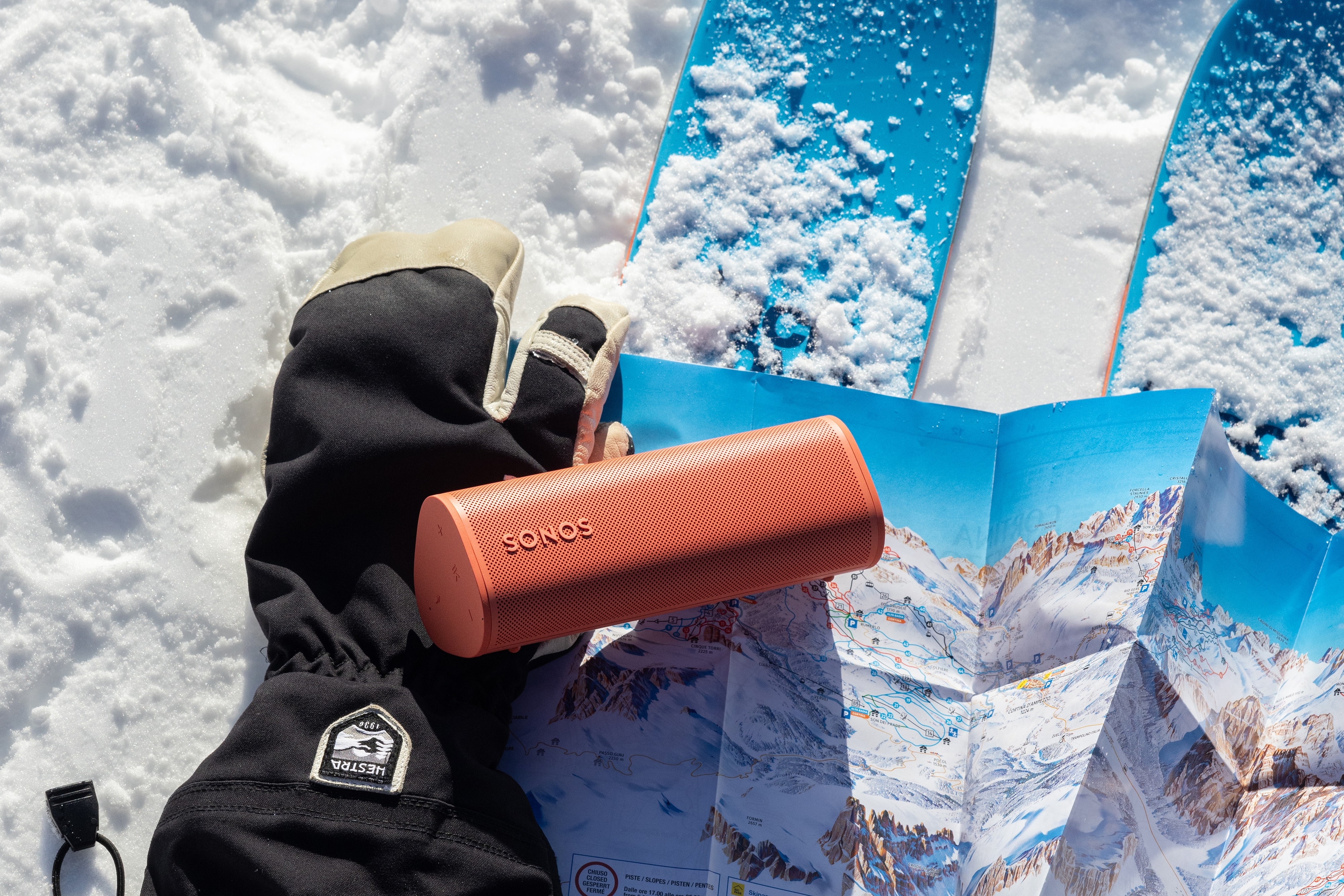 Ein Roam 2 in Rot auf einem Handschuh mit Skiern im Schnee