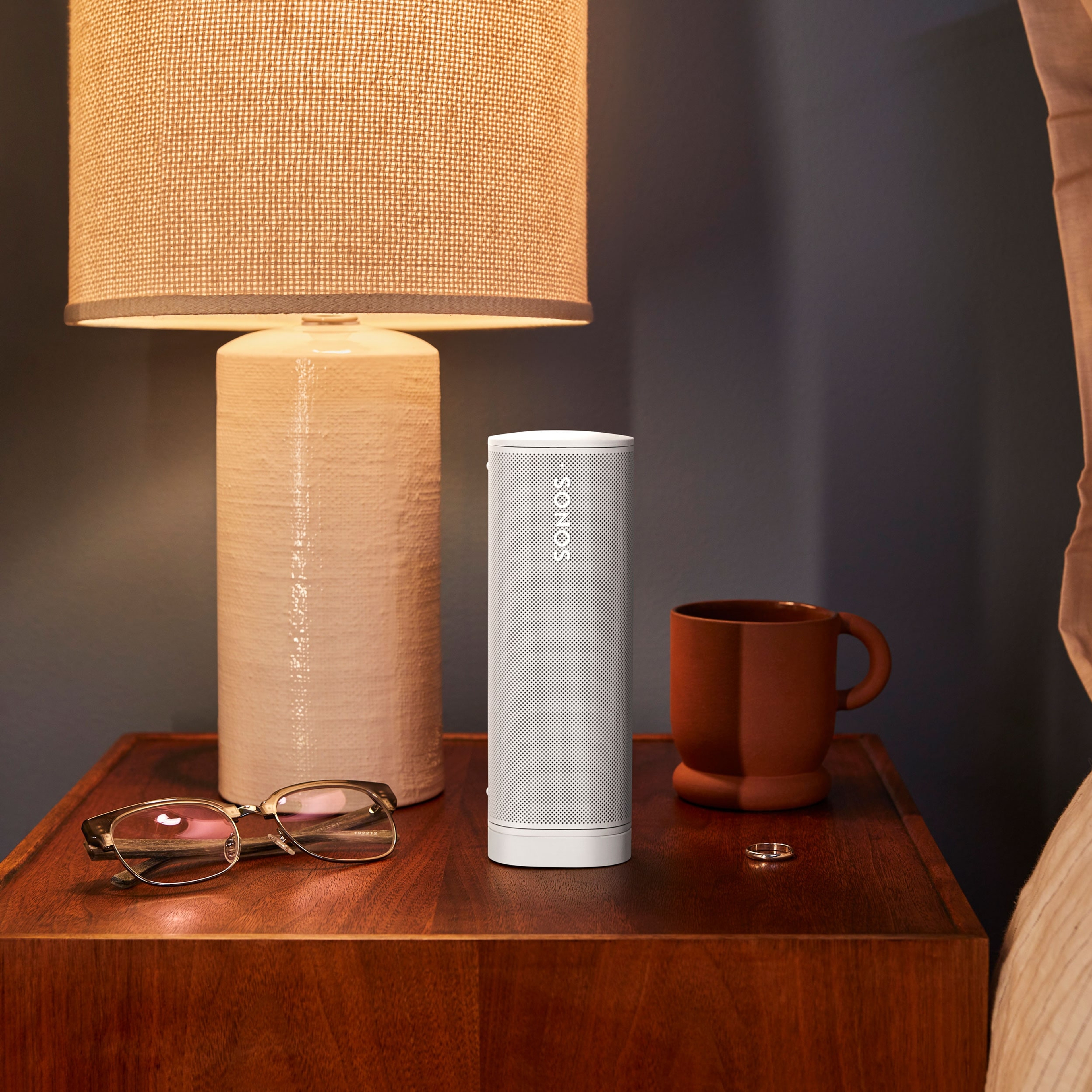 Ein Sonos Roam 2 in Weiß auf einem Nachttisch neben einer Lampe