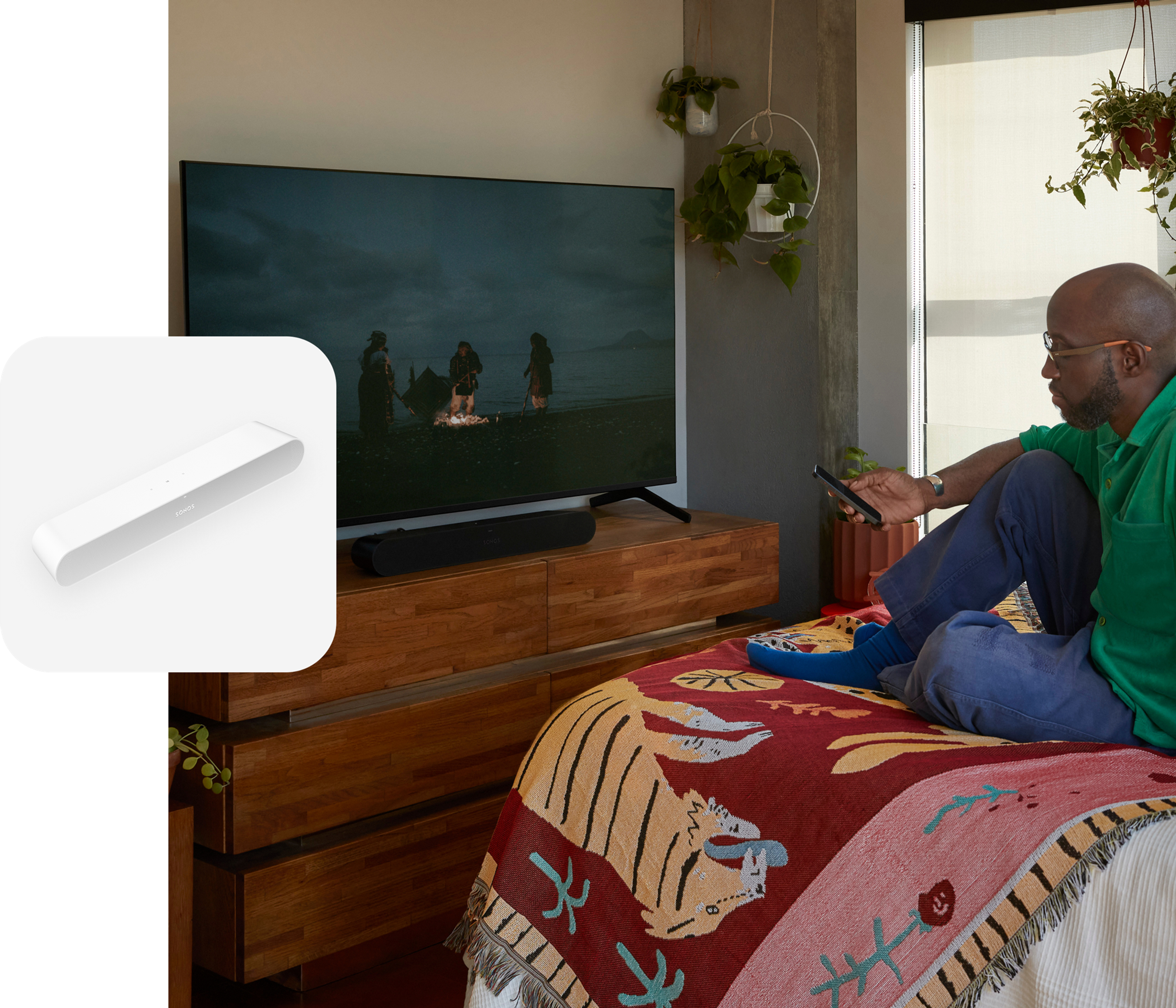 User sitting on their bed watching a film with sound from a black Ray soundbar