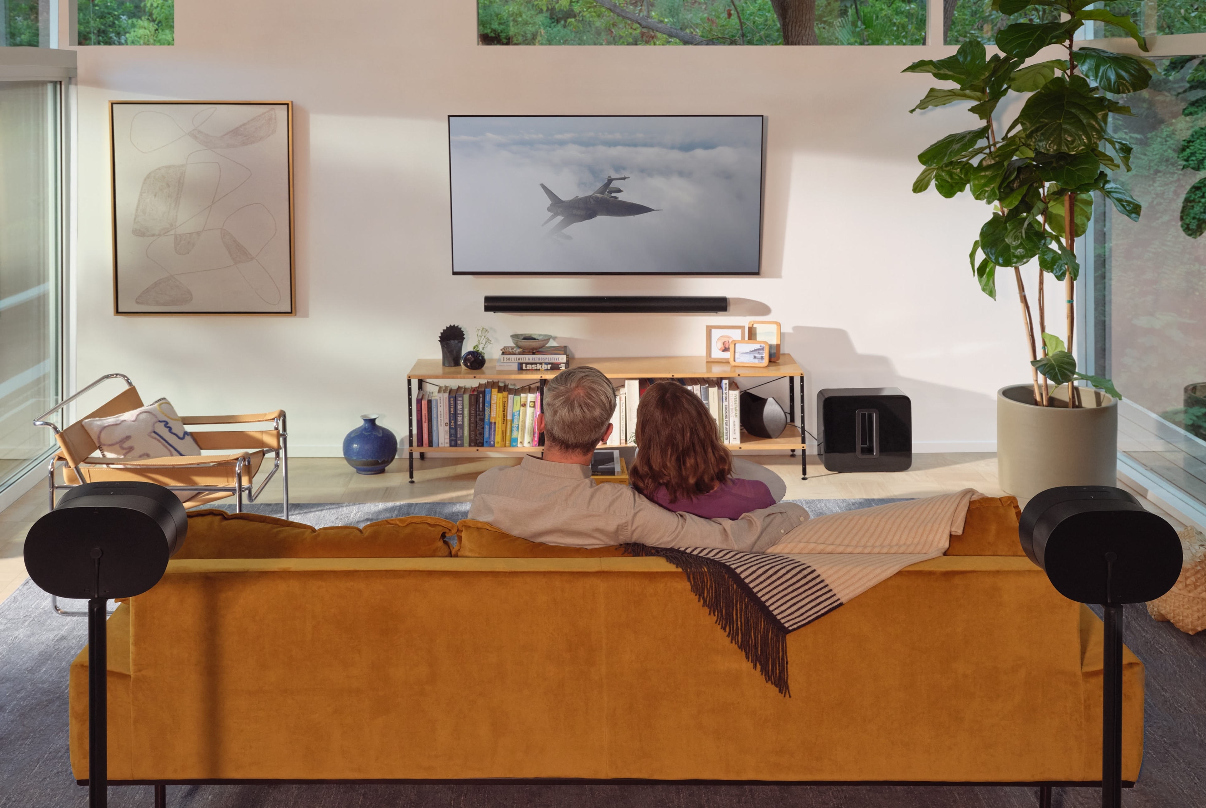 Ett par som sitter i soffan och lyssnar på två vita Sonos Era 300-högtalare