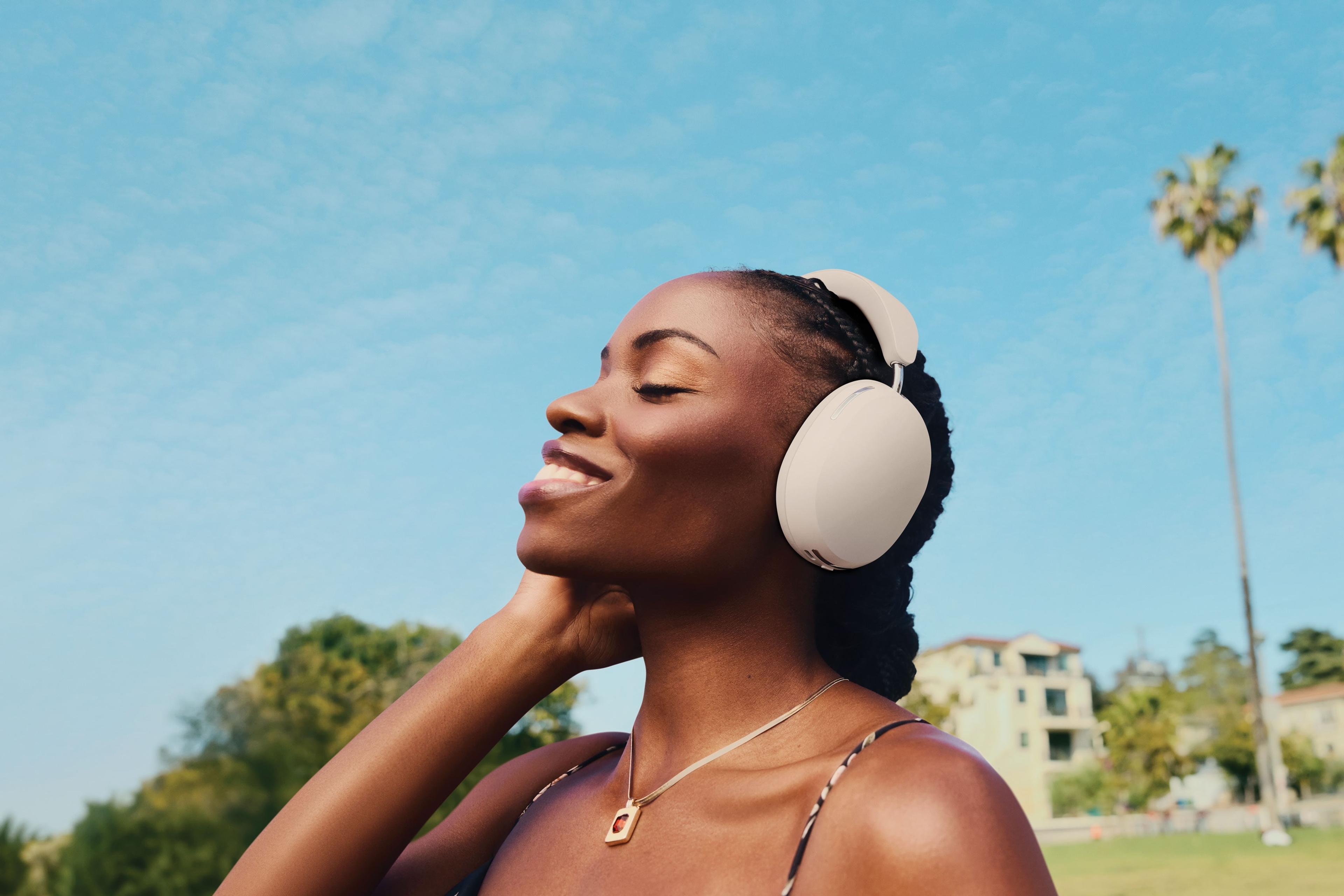 Person outside listening to music on white Sonos Ace headphones with blue sky and palm trees in the background